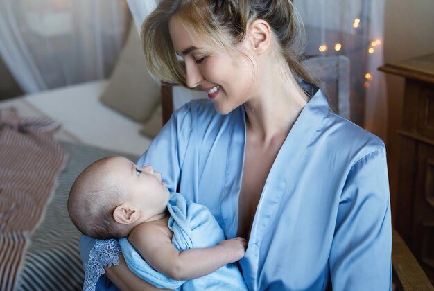 Foto portret van jonge mooie moeder met haar schattige kleine baby gewikkeld in de blauwe doek