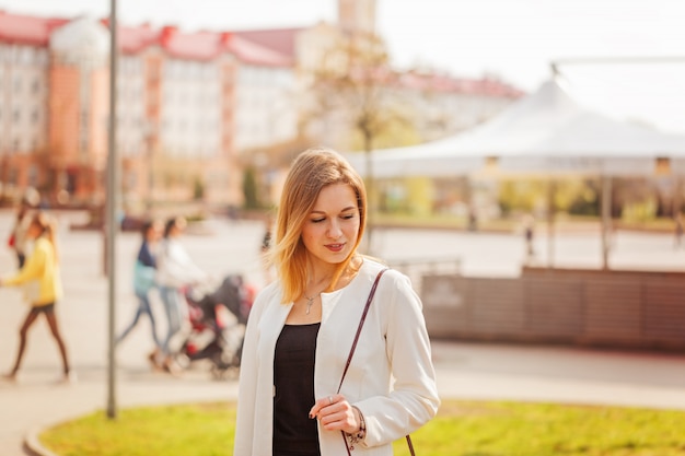 Portret van jonge mooie vrouw die aan camera in stad bij bulding achtergrond in zonnige de lentedag glimlachen