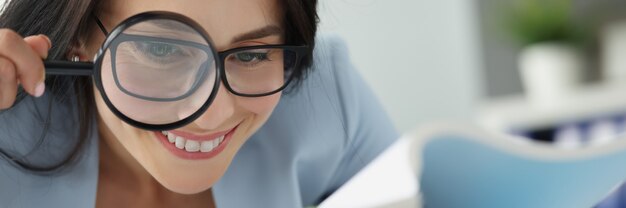 Portret van jonge mooie vrouw die documenten door vergrootglas onderzoekt