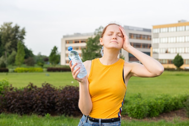 Portret van jonge mooie vrouw die gele t-shirt draagt die een fles water houdt