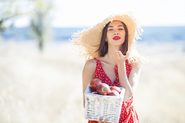 Portret van jonge mooie vrouw die strohoed in de zomer draagt. Vrouw met verse appels op de natuur.