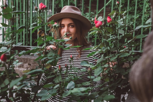 Portret van jonge mooie vrouw in hoed in de buurt van roze bloemen