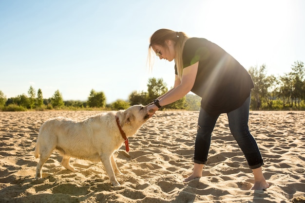 Portret van jonge mooie vrouw in zonnebril zittend op zandstrand met golden retriever hond meisje...