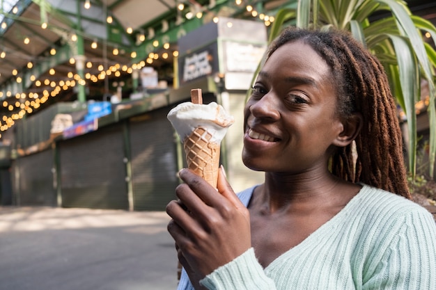 Foto portret van jonge mooie vrouw met afro-dreadlocks die van een ijsje in de stad genieten