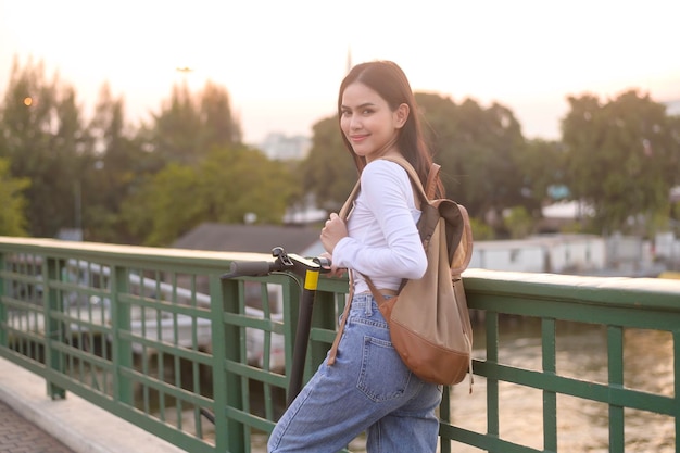 Portret van jonge mooie vrouw met een elektrische scooter over brug in moderne stadsachtergrond