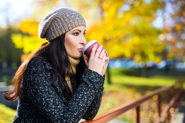 Portret van jonge mooie vrouw met koffiekopje wandelen in herfst park