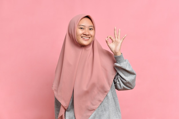 Portret van jonge moslimvrouw die ok teken toont tegen op roze background