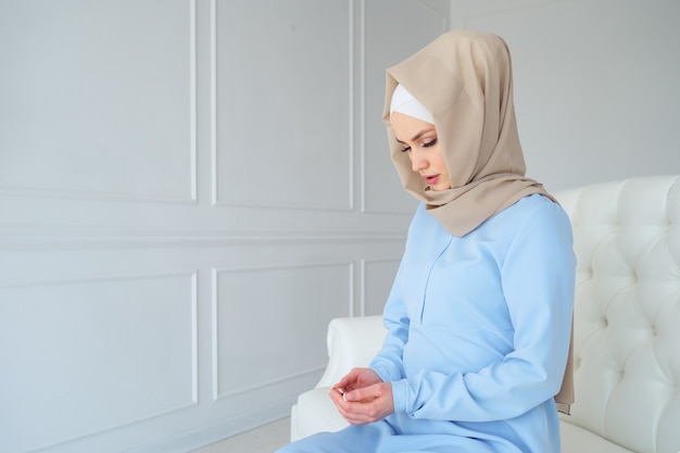 Portret van jonge moslimvrouw in beige hijab en traditionele kleding bidden