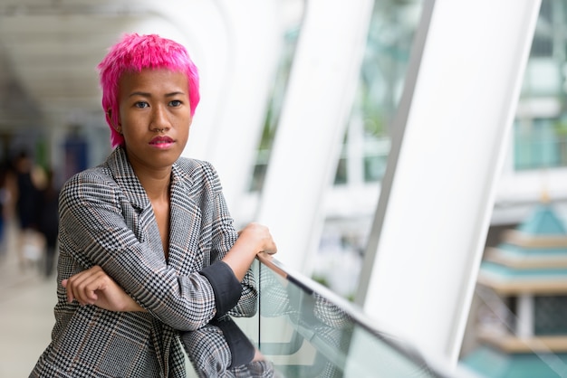 Portret van jonge opstandige Aziatische zakenvrouw met roze haren op loopbrug in de stad buiten