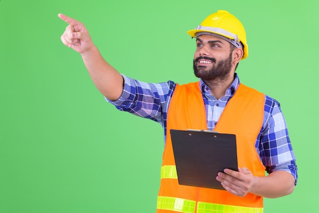 Portret van jonge overgewicht bebaarde Indiase man bouwvakker tegen Chromakey met groene muur