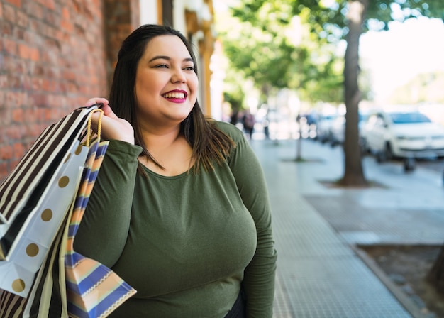 Portret van jonge plus size vrouw met boodschappentassen buiten op straat