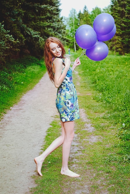 Portret van jonge roodharige vrouw in de lentetuin met sproeten. Paarse ballonnen. Verjaardag, vakantie