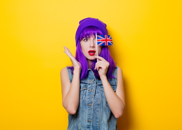 Portret van jonge stijl hipster meisje met paars haar en de vlag van Groot-Brittannië in de hand op gele achtergrond