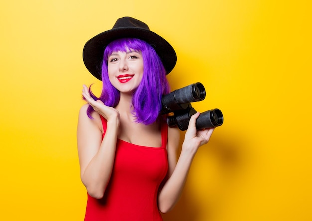 Portret van jonge stijl hipster meisje met paars kapsel en verrekijker op gele achtergrond