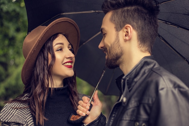 Portret van jonge verliefde paar wandelen in het stadspark en paraplu gebruiken om de regen te beschutten Heteroseksuele geliefden hebben een datum samen tijd doorbrengen in bewolkte regenachtige dag met emoties