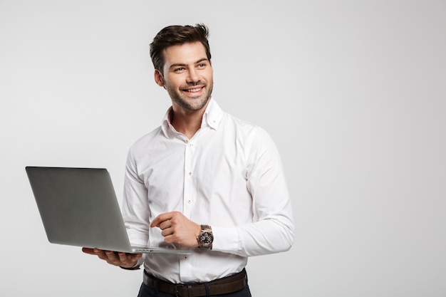 Portret van jonge vrolijke zakenman in polshorloge die laptop vasthoudt en gebruikt die op wit wordt geïsoleerd