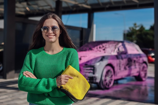 Portret van jonge vrouw in groene trui met gele microvezeldoek en auto die bedekt is met speld