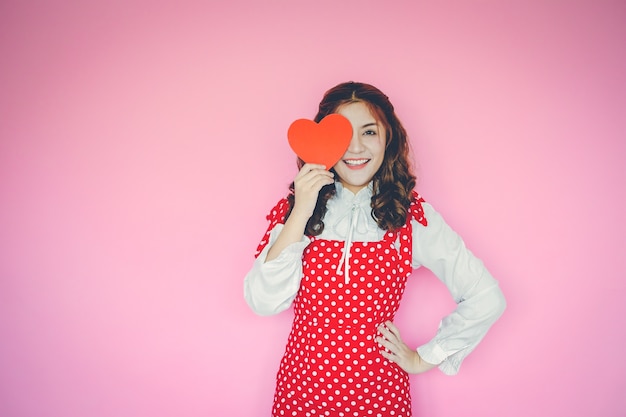 Portret van jonge vrouw met rood hart voor haar ogen op roze achtergrond