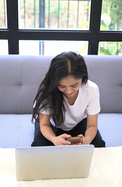 Portret van jonge vrouwelijke freelance werken met laptopcomputer en het gebruik van mobiele telefoon in de woonkamer.