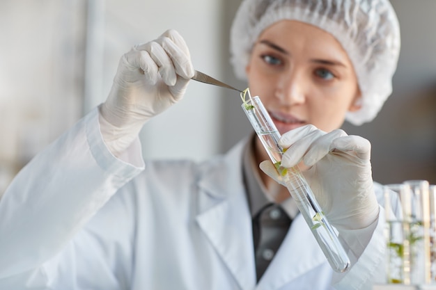 Portret van jonge vrouwelijke wetenschapper reageerbuis met plantmonsters houden tijdens het werken aan onderzoek in biotechnologie lab, kopie ruimte close-up