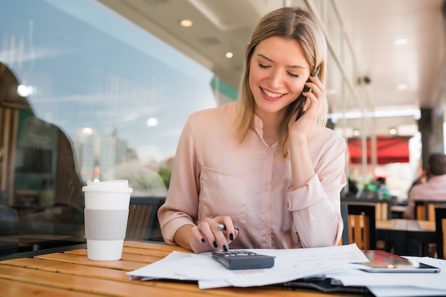 Portret van jonge zakenvrouw praten aan de telefoon tijdens het werken bij coffeeshop. bedrijfsconcept.
