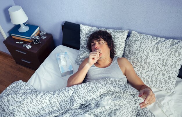 Portret van jonge zieke man hoesten liggend op bed. Ziekte en gezondheidszorg concept.