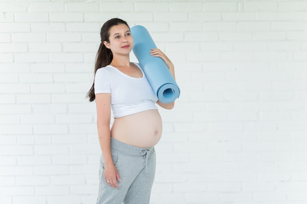 Portret van jonge zwangere vrouw met yogamat