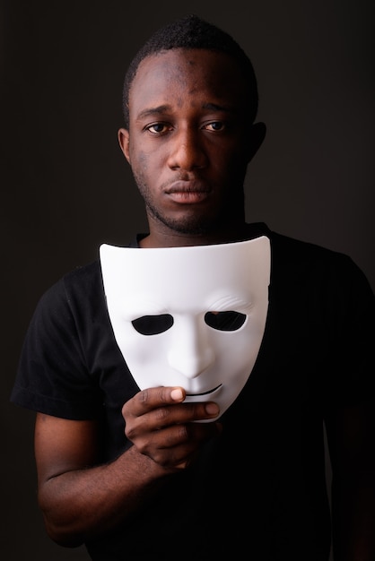 Portret van jonge zwarte Afrikaanse man in het masker van de donkere kamerholding