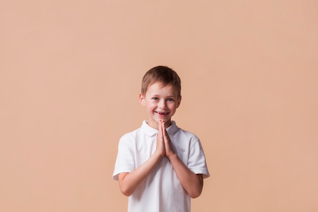 Portret van jongen die met een glimlach op zijn gezicht over beige achtergrond bidt