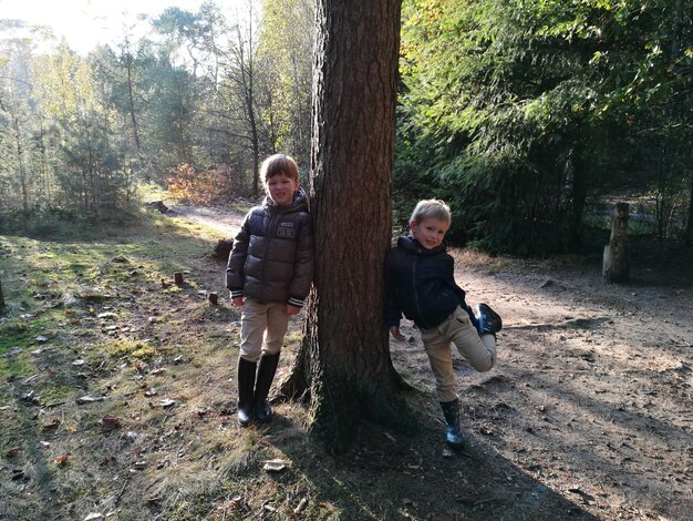 Foto portret van jongens die leunen op een boom in het bos