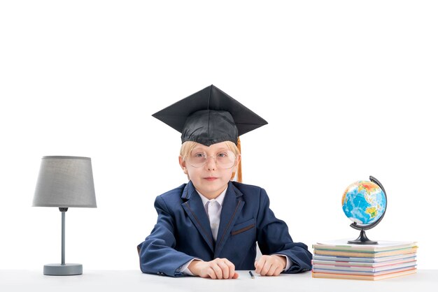 Portret van kind in schooluniform en studentenhoed aan tafel naast notitieboekjes en wereldbol Onderwijs op lagere school in het buitenland