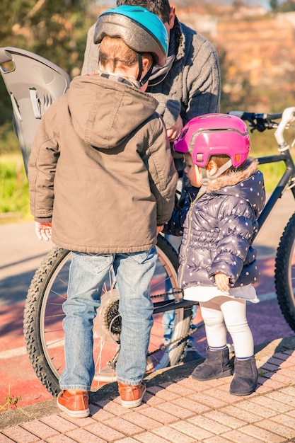 Portret van kinderen met een veiligheidshelm die naar hun vader kijken terwijl ze een beschadigde fietsband repareren