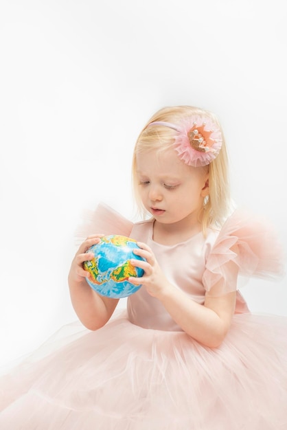Portret van klein meisje in roze jurk met decoratie hoepel houdt wereldbol model in handen Blond meisje witte achtergrond