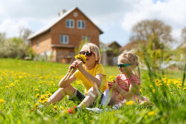 Portret van kleine blonde jongen en meisje met boeket paardebloemen Broer en zus in de wei bij het huis