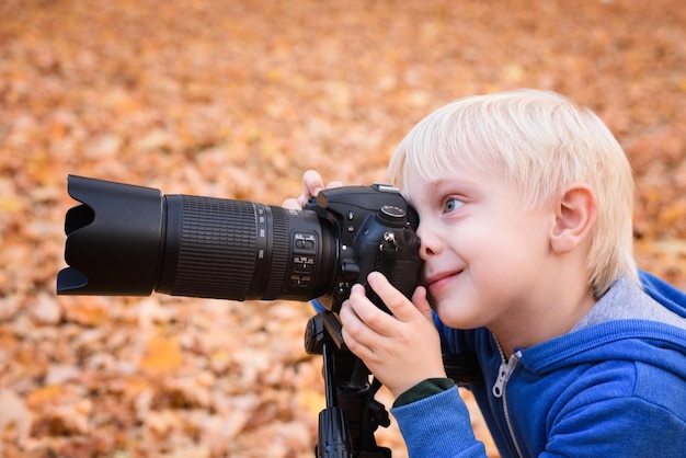 Portret van kleine blonde jongen maakt foto's op een spiegelreflexcamera Autumn Park