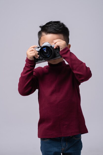 Portret van kleine jongen die rode sweater draagt die status geïsoleerd op grijs draagt