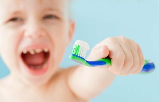 Portret van kleine jongen met tandenborstel op blauwe achtergrond