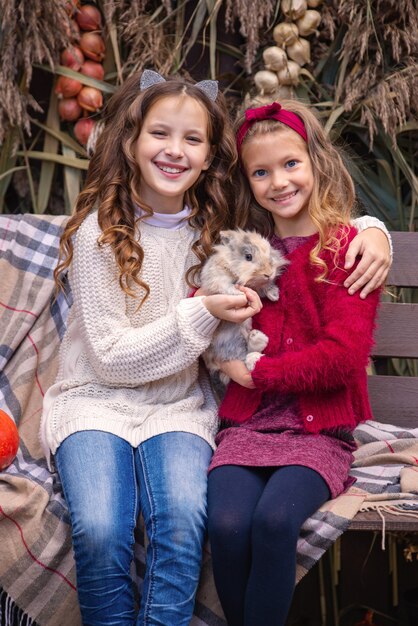 portret van kleine meisjes vriendinnen in de herfst met een konijn in hun handen in de buurt van hun huis fam