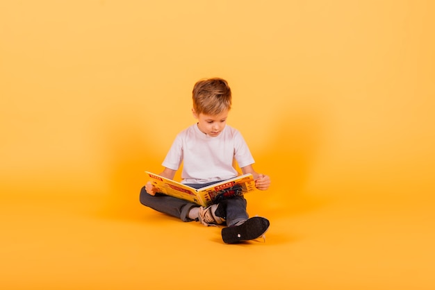 Portret van kleine schooljongen met boek op gele achtergrond, studio