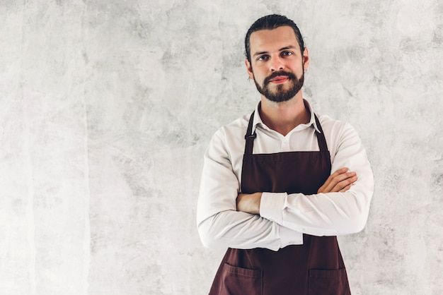 Portret van knappe bebaarde barista man kleine ondernemer glimlachen op de muur