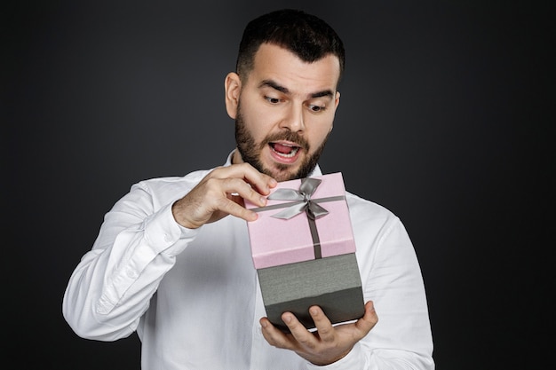 Portret van knappe bebaarde man in wit overhemd opent geschenkdoos geïsoleerd op zwarte achtergrond