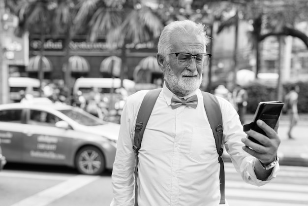 Portret van knappe bebaarde senior toeristische man stijlvolle kleding dragen tijdens het verkennen van de stad bangkok in zwart-wit