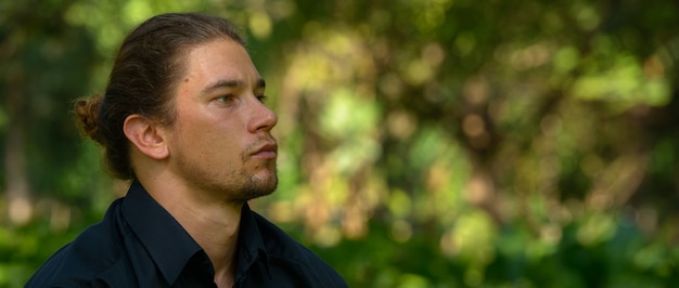 Portret van knappe bebaarde zakenman met lang haar ontspannen in het park buiten