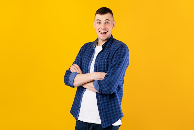 Portret van knappe blanke man lachend naar de camera poseren met gevouwen armen over gele studio achtergrond