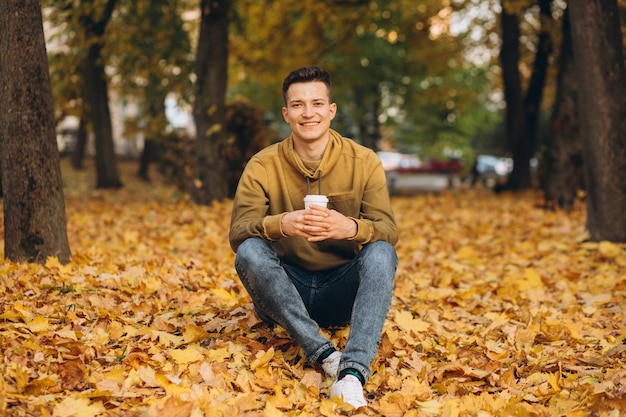 Portret van knappe en gelukkige jongen glimlachend en koffie drinken in de herfst park