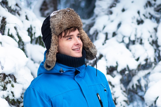 Portret van knappe jonge gelukkig man in winterkleren met hoed met oorkleppen