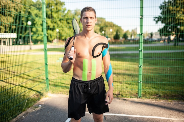 Portret van knappe jonge Kaukasische professionele tennisspeler met elastische banden op lichaam dragende racket