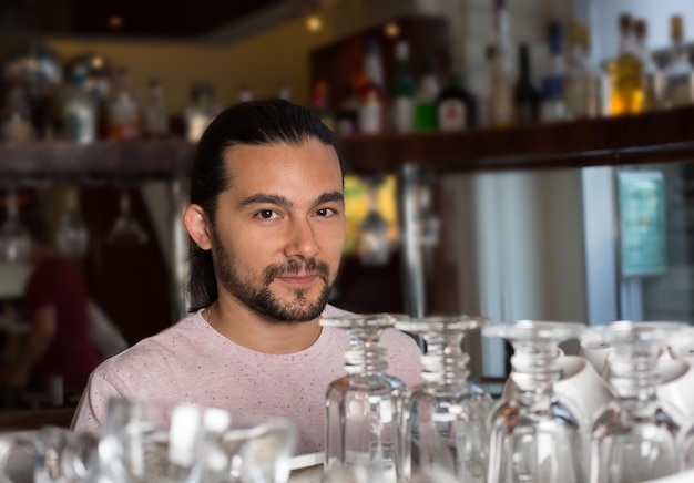 Portret van knappe jonge lachende barman achter de toog met cocktailglazen, wazige achtergrond.