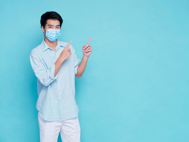 Portret van knappe jonge man met medische masker in casual kleding vinger omhoog. concept covid 19