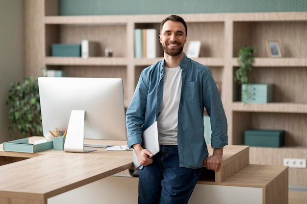 Portret van knappe jonge zakenman die laptop vasthoudt en poseert in kantoorinterieur